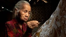 Seorang ibu penjual makanan tradisional tersenyum optimis di pasar, merefleksikan semangat ketahanan ekonomi masyarakat Indonesia. Senyumnya menggambarkan harapan dan upaya gigih dalam merajut kehidupan yang lebih baik.
