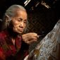 Seorang ibu penjual makanan tradisional tersenyum optimis di pasar, merefleksikan semangat ketahanan ekonomi masyarakat Indonesia. Senyumnya menggambarkan harapan dan upaya gigih dalam merajut kehidupan yang lebih baik.