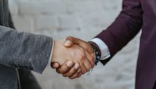 Dua orang berjabat tangan di atas meja yang penuh dengan dokumen, melambangkan kesepakatan bisnis yang kuat dan kolaborasi yang menguntungkan melalui sistem bagi hasil. Ini menunjukkan komitmen bersama untuk mencapai kesuksesan finansial yang adil dan transparan bagi semua pihak terlibat.