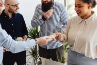 Sekelompok orang yang bersemangat berkolaborasi di meja diskusi, tampak sedang merancang strategi bisnis mereka dengan penuh antusiasme. Tumpukan koin di tengah menunjukkan konsep patungan modal sebagai fondasi utama untuk mewujudkan impian usaha bersama.