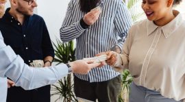 Sekelompok orang yang bersemangat berkolaborasi di meja diskusi, tampak sedang merancang strategi bisnis mereka dengan penuh antusiasme. Tumpukan koin di tengah menunjukkan konsep patungan modal sebagai fondasi utama untuk mewujudkan impian usaha bersama.