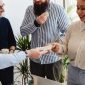 Sekelompok orang yang bersemangat berkolaborasi di meja diskusi, tampak sedang merancang strategi bisnis mereka dengan penuh antusiasme. Tumpukan koin di tengah menunjukkan konsep patungan modal sebagai fondasi utama untuk mewujudkan impian usaha bersama.