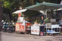 Seorang ibu rumah tangga sedang memilih sayuran di pasar tradisional Indonesia, mencerminkan aktivitas ekonomi sehari-hari serta tantangan dalam memenuhi kebutuhan pokok keluarga. Pasar seperti ini menjadi jantung perekonomian lokal, tempat transaksi dan interaksi sosial yang dinamis terjadi.