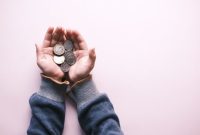 Sejumlah tangan secara simbolis saling menggenggam koin, melambangkan semangat gotong royong dan kebersamaan dalam praktik simpan pinjam. Gambar ini merepresentasikan bagaimana setiap individu berkontribusi untuk menciptakan kekuatan finansial kolektif yang saling mendukung.